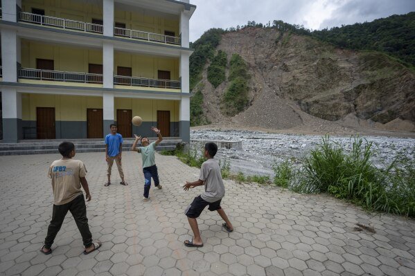 Children play volleyball with a landslide-damaged hill visible in the background at Saraswati Secondary School in Gyalthum, Melamchi, northeast of Kathmandu, Nepal on Saturday, Sept. 14, 2024. (AP Photo/Niranjan Shrestha)