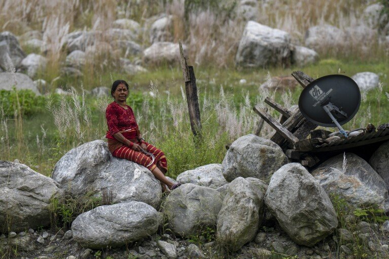 Suntali Jyoti, 56, sits where her house and field once stood, in Chanaute, Melamchi, northeast from Kathmandu, Nepal, Sunday, Sept. 15, 2024, now covered with large rocks brought by floods in 2021. (AP Photo/Niranjan Shrestha)