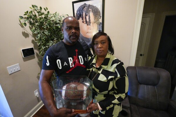 Phillip Laster Sr. and his wife Ashanta Laster hold a football signed by teammates of their son Phillip Laster Jr., in Brandon, Miss., Tuesday, Aug. 27, 2024, that was given to them on senior night after Laster Jr.'s passing. A portrait of Laster Jr. is behind them. (AP Photo/Gerald Herbert)