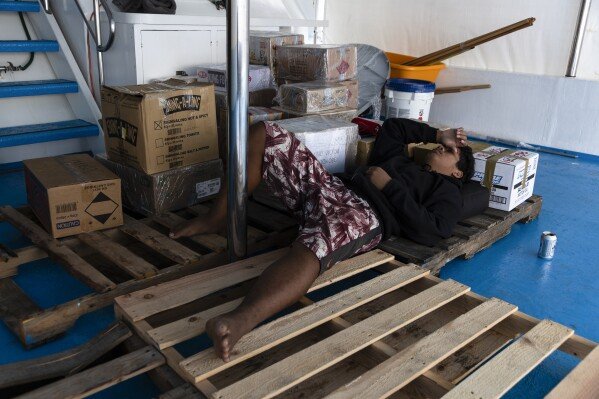 Maxson Blesson sleeps on a wooden pallets on the top deck of the Ryoma, a boat that brings goods through the Pacific Ocean to Helen Island, Palau, on July 15, 2024. (AP Photo/Yannick Peterhans)