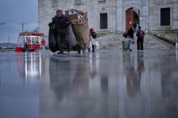 A man pulls his cart full of discarded cartons past Yeni mosque on a rainy day in Istanbul, Turkey, Wednesday, Feb. 5, 2025. (AP Photo/Francisco Seco)
