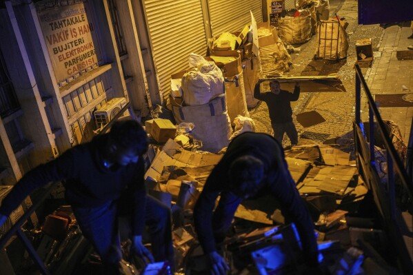 Veysel Dogan, right, and his two sons Ergin, left, and Murtaza load a lorry with discarded cartons at Eminonu commercial area in Istanbul, Turkey, Tuesday, Feb. 26, 2025. (AP Photo/Francisco Seco)