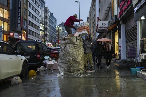 A paper collector is helped to load his cart with discarded carton boxes at Kadikoy neighborhood in Istanbul, Turkey, Monday, Feb. 10, 2025. (AP Photo/Francisco Seco)
